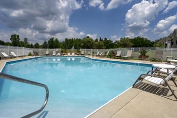 A large outdoor swimming pool surrounded by a metal fence and lounge chairs.